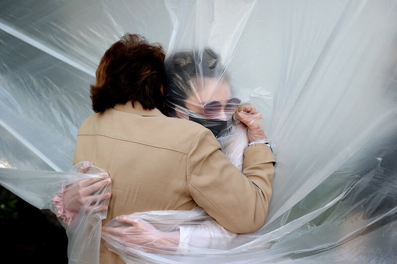 24 Μαΐου: Η Olivia Grant, δεξιά, αγκαλιάζει τη γιαγιά της, Mary Grace Sileo, μέσα από ένα πλαστικό πανί, Νέα Υόρκη. Βλέπουν η μία την άλλη για πρώτη φορά από την έναρξη της πανδημίας.