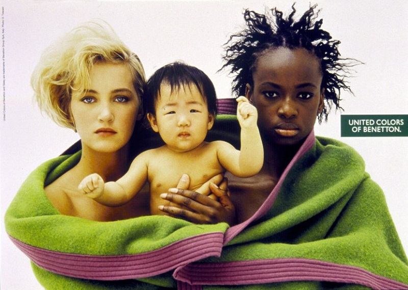 Δύο γυναίκες κρατούν ενωμένες ένα μωρό, διαφορετικών χρωμάτων και οι τρεις άνθρωποι, σκεπασμένοι με μία κουβέρτα. Πρώτη καμπάνια για την προάσπιση της ομόφυλης σεξουαλικότητας, 1991. 